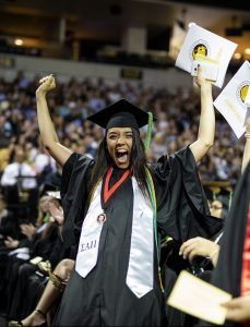 A woman in cap and gown raising her hands in celebration after receiving her diploma at the UCF Arena